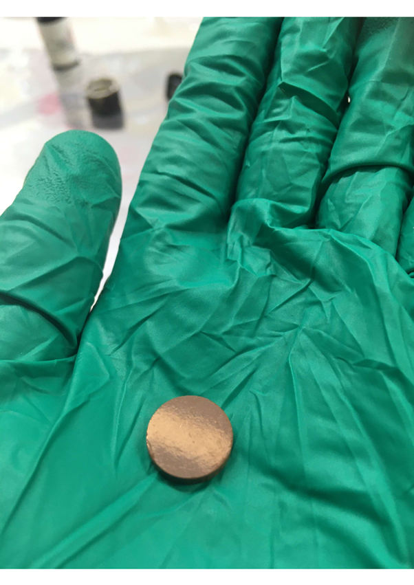 Small gold looking dish held in gloved hand.